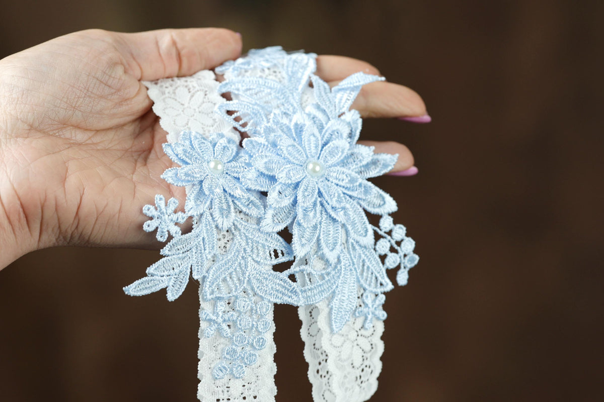 A hand holding a piece of delicate blue lace with white floral patterns.