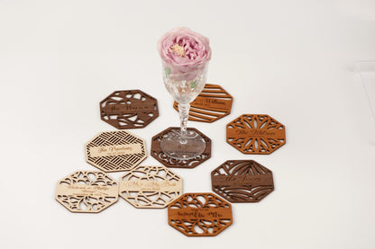 a glass vase with a pink flower, surrounded by various coasters and wooden coasters with text on them.