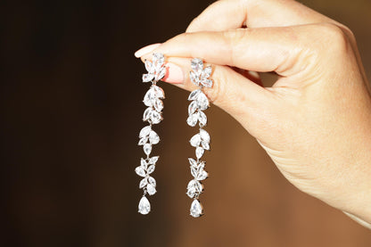 A hand holding a pair of elegant diamond earrings with multiple dangling branches.