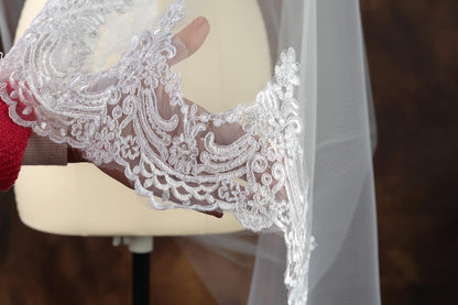A hand holding a delicate white lace veil with intricate floral patterns.