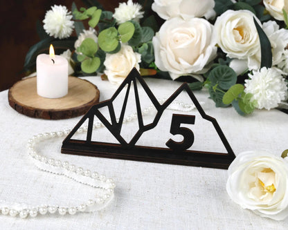a wooden sign with the number "5" on it, surrounded by white flowers and a lit candle on a table.