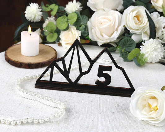 a wooden sign with the number "5" on it, surrounded by white flowers and a lit candle on a table.