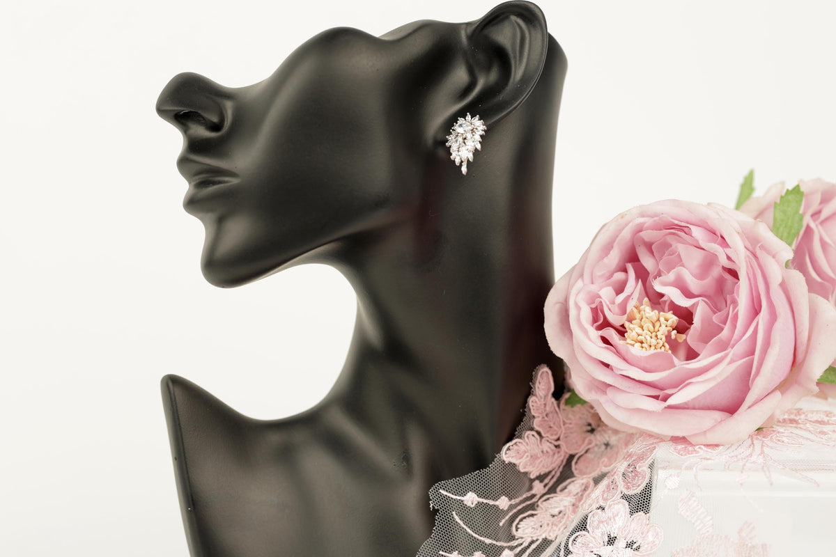 A black mannequin head wearing a pair of diamond earrings, with a pink rose placed next to it.