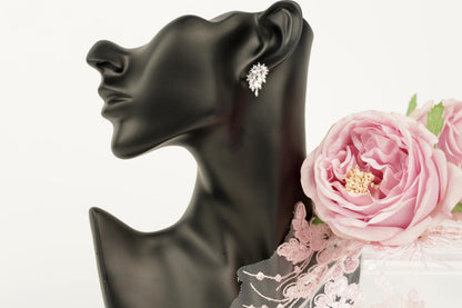 A black mannequin head wearing a pair of diamond earrings, with a pink rose placed next to it.