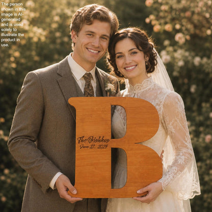 A happy couple, dressed in formal attire, smiling and holding a large wooden letter 'B' with the text "The Bishes" and "June 21, 2029" written on it.