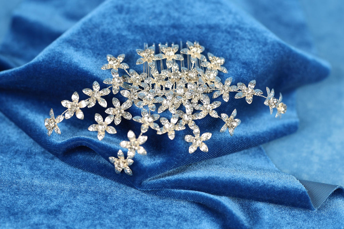 A close-up view of a decorative hair accessory, possibly a hair clip or headband, with numerous small, sparkling crystal or gemstone elements arranged in a floral pattern on a blue velvet background.