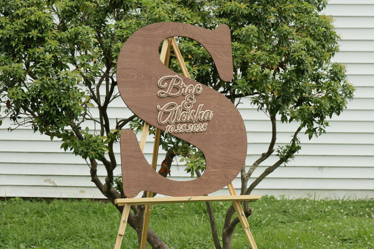 A wooden sign with the letters 'S' and 'A' on it, standing on a wooden stand in front of a tree.