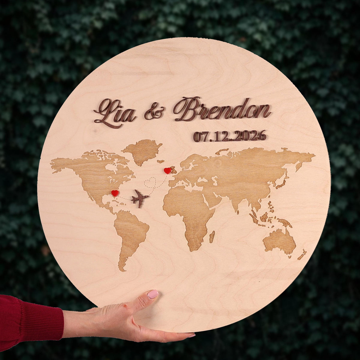 A person is holding a wooden sign with a world map and the names 'Lia & Brandon' written on it.