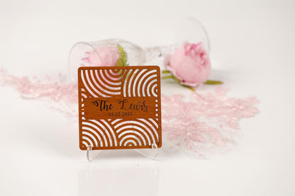 a wooden coaster with a decorative design, placed on a white surface next to a glass of wine and a pink rose.
