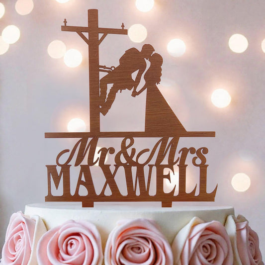 A wooden cake topper with a silhouette of a man and a woman kissing, along with the text "Mr & Mrs MAXWELL" on it.