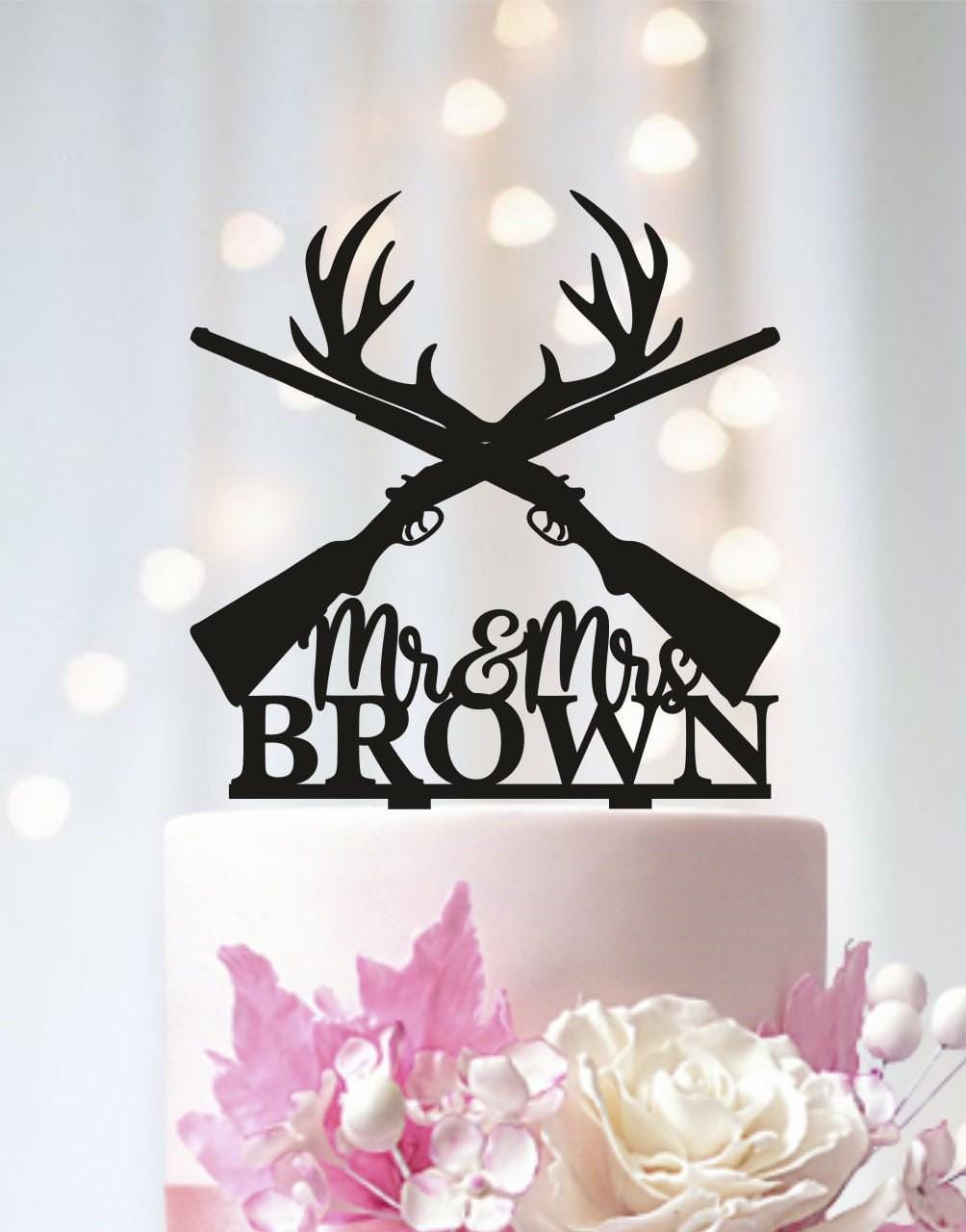 A black silhouette of a crossed rifle with antlers on top of a white wedding cake, with the text "Mr & Mrs Brown" below it.