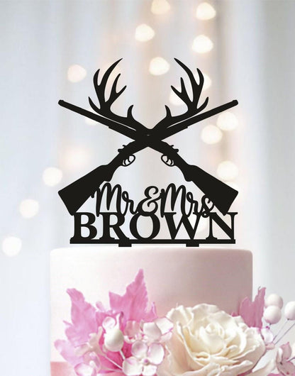 A black silhouette of a crossed rifle with antlers on top of a white wedding cake, with the text "Mr & Mrs Brown" below it.
