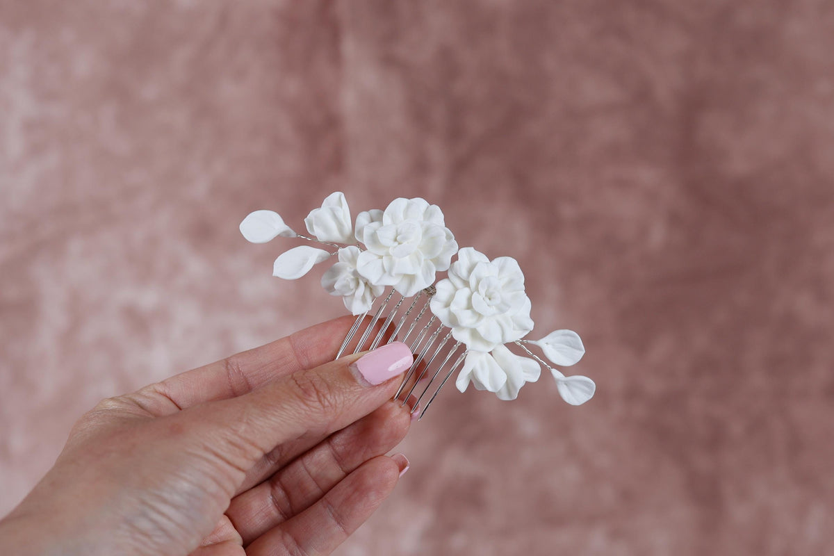 A hand holding a white flower hair accessory against a pink background.