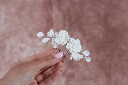 A hand holding a white flower hair accessory against a pink background.