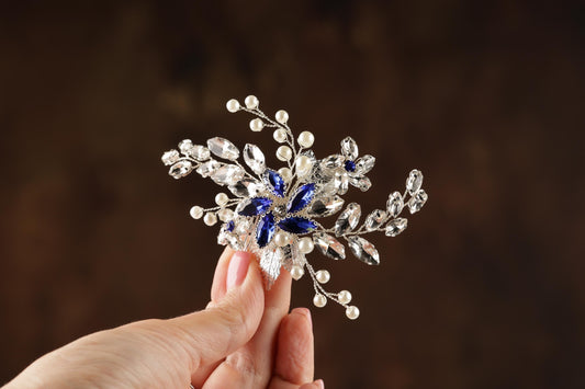 A hand holding a decorative piece of jewelry, which appears to be a brooch or headband, against a dark background.