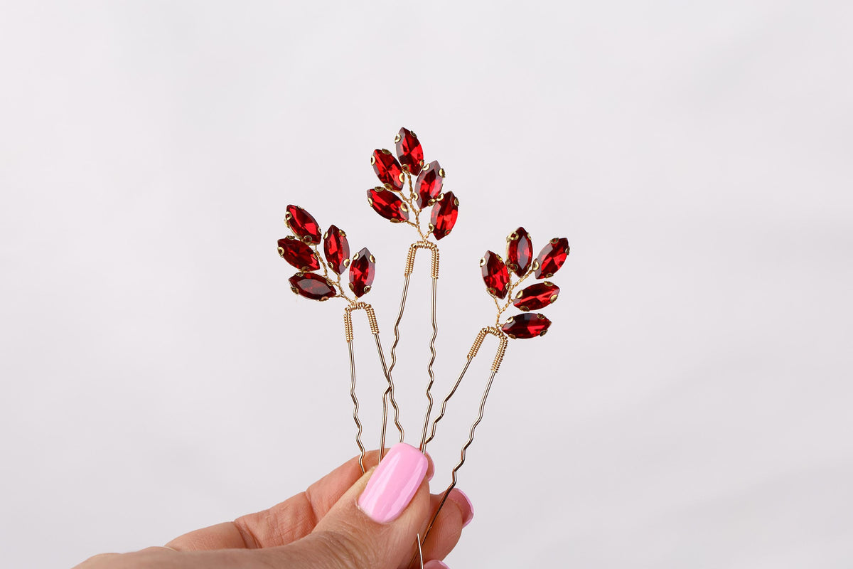 a hand holding a pair of red crystal hair pins