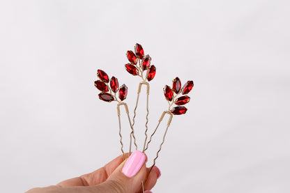 a hand holding a pair of red crystal hair pins