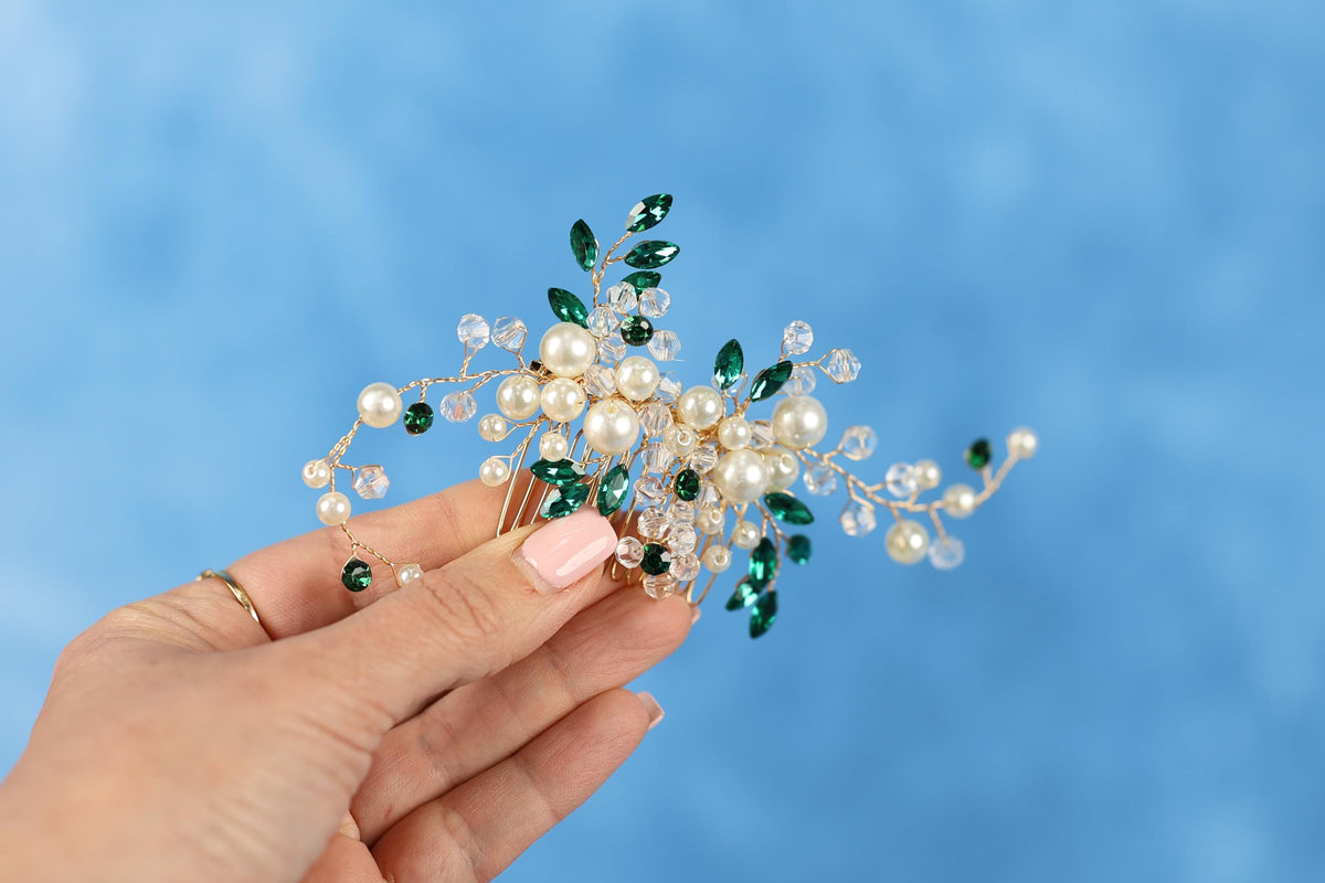 A hand holding a decorative hair accessory with green and white elements against a blue background.