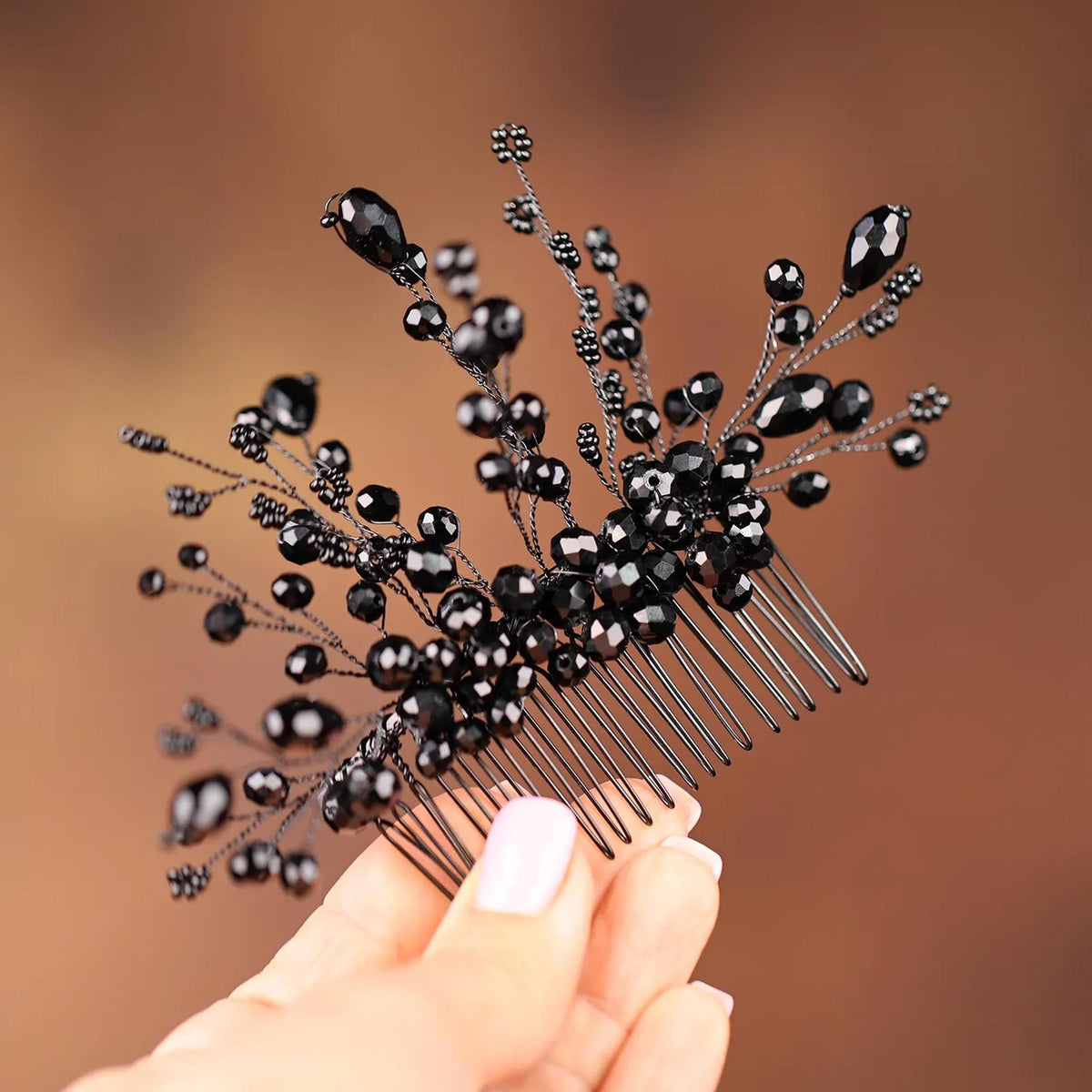 A close-up image of a person's hand holding a black hair accessory with black beads or beads attached to it.