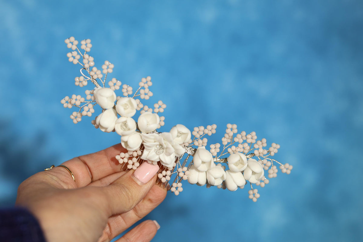 A hand holding a delicate, white flower-like accessory against a blue background.