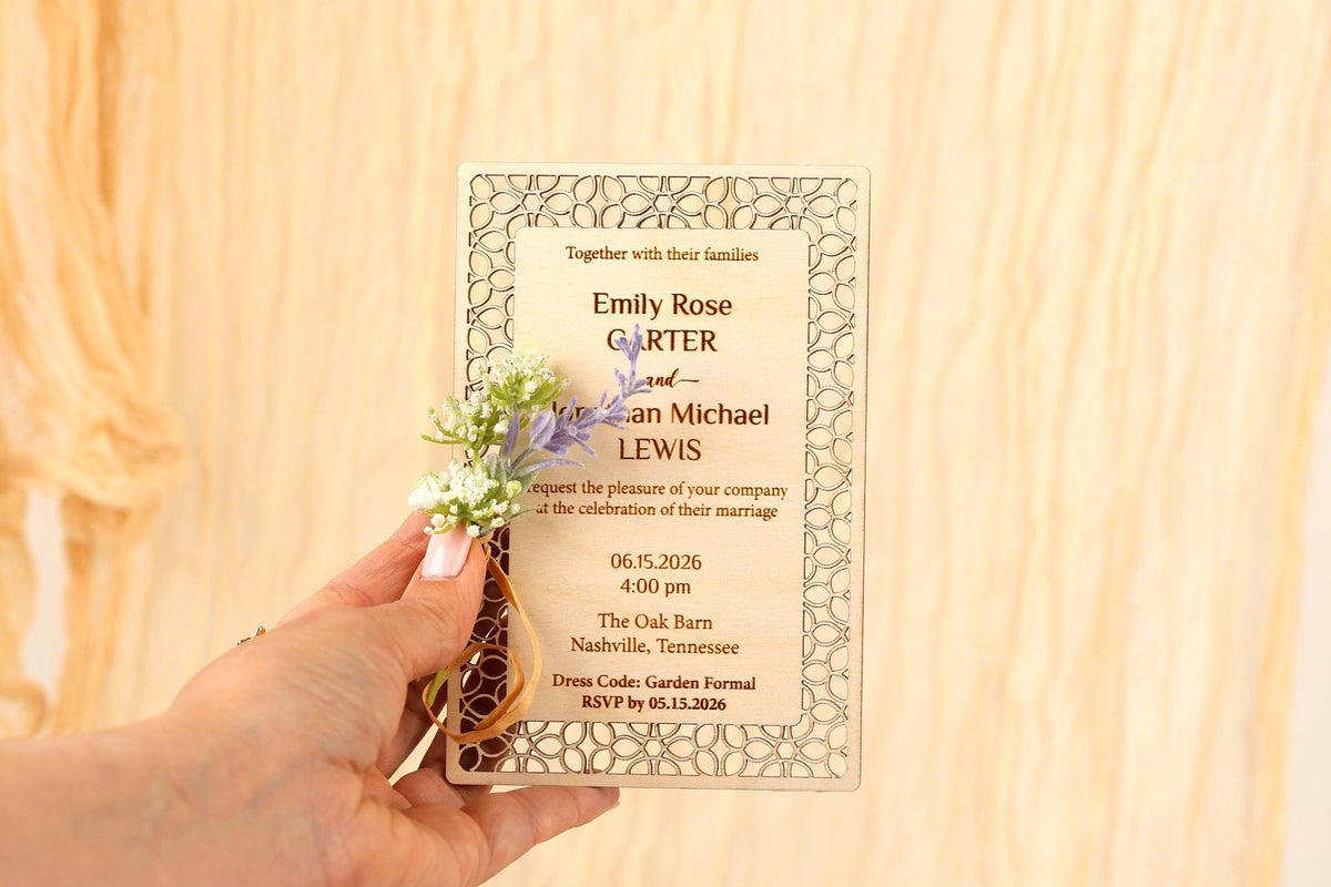 a hand holding a wedding invitation card with floral decorations.