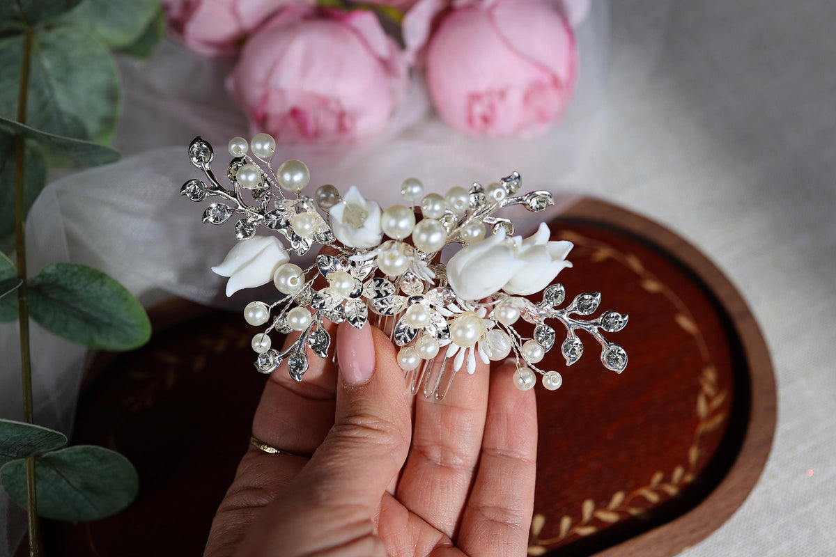 A hand holding a decorative hair clip with white flowers and pearls.