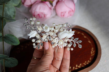 A hand holding a decorative hair clip with white flowers and pearls.