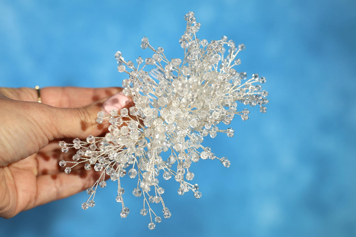 A hand holding a cluster of small, clear crystal branches against a blue background.