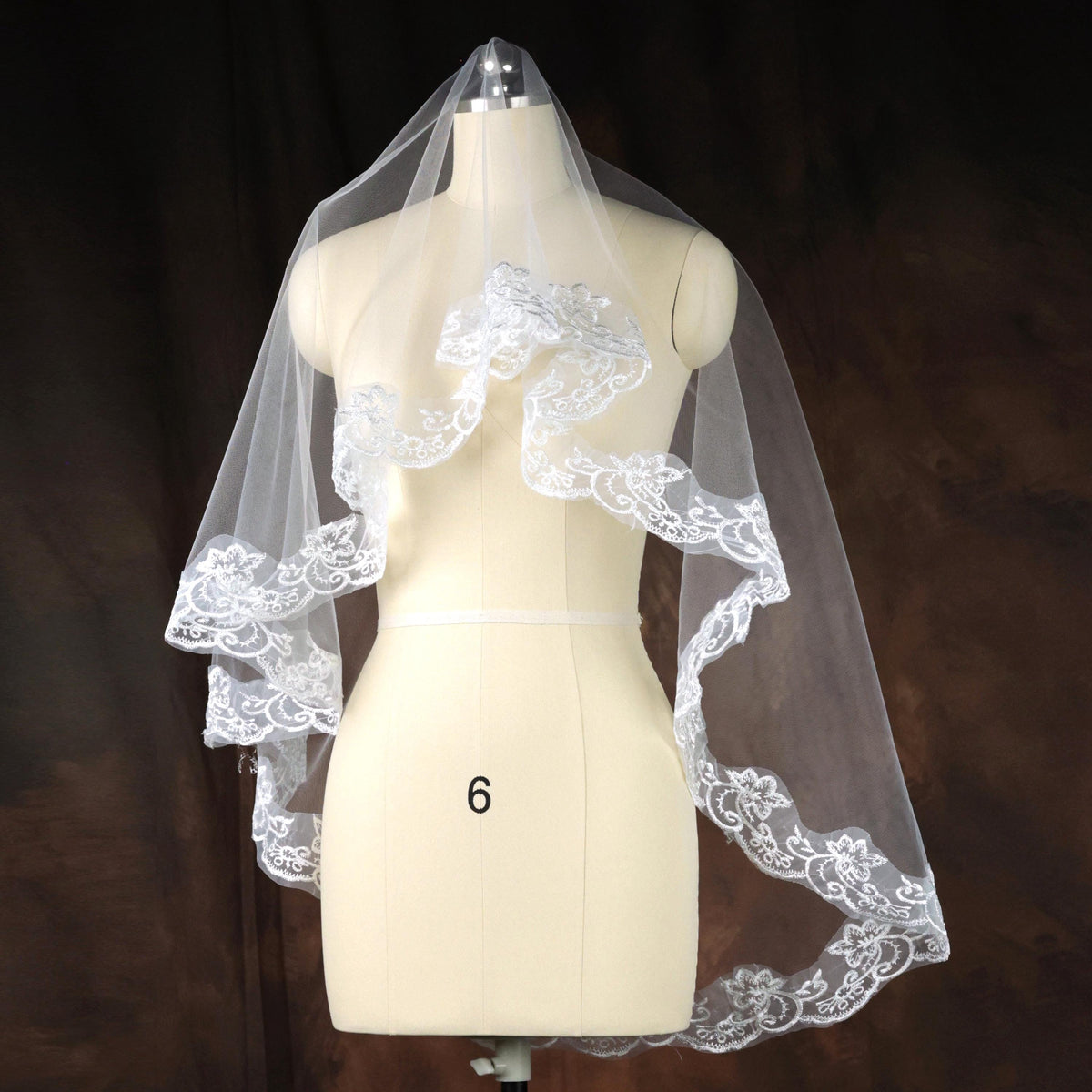 A white wedding veil with a delicate lace design is displayed on a mannequin.