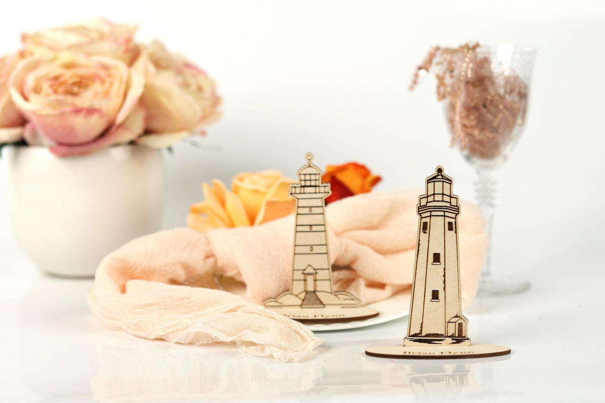 a white vase with pink roses, a wooden lighthouse, and a glass vase with a bouquet of flowers, all placed on a white surface.