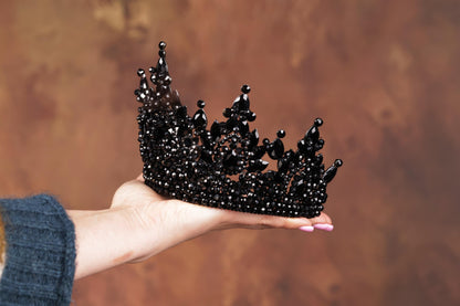 a hand holding a black crown on a brown background