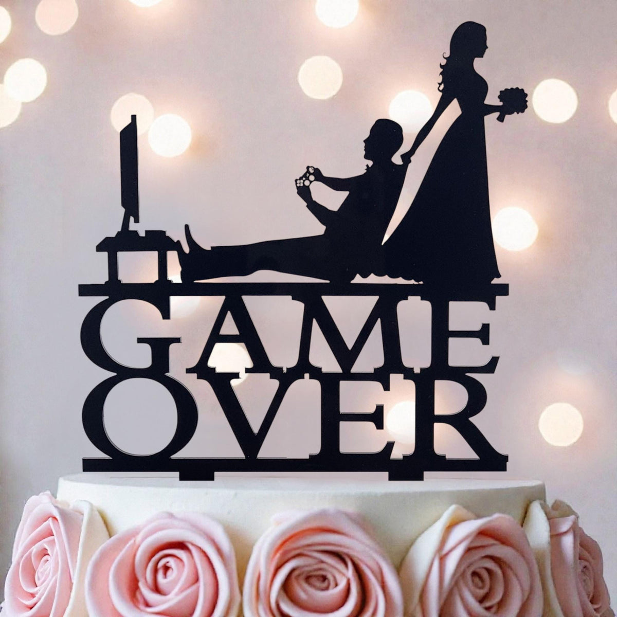 A silhouette of a bride and groom playing a video game on a cake topper, with the words "GAME OVER" written on it.