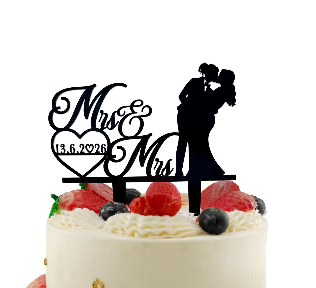 A black silhouette of a bride and groom on top of a white wedding cake, with the words "Mrs & Mrs" and the date "13.6.2026" written on the cake topper.