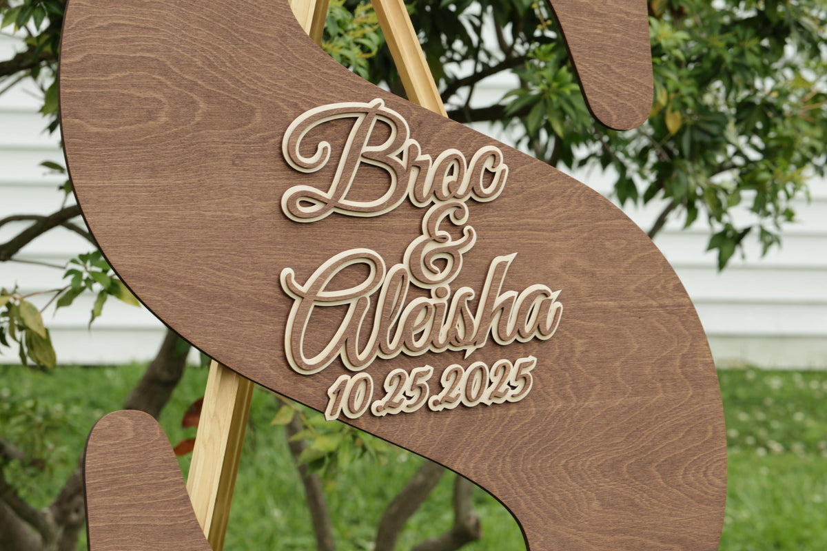 A wooden sign with the names "Bico & Alisha" and the date "10.25.2025" carved into it.