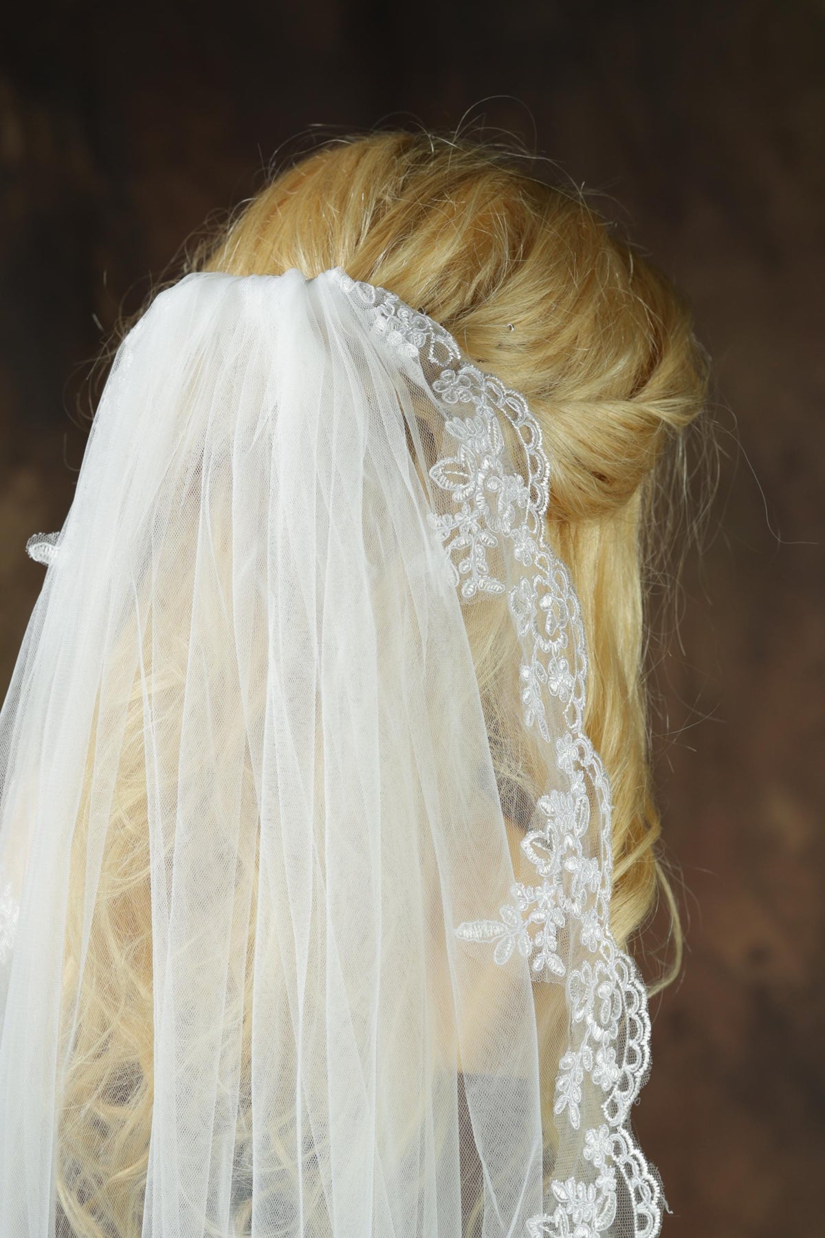 A close-up view of a person's head wearing a white veil with intricate lace detailing.