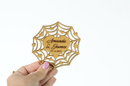 A hand holding a wooden wedding invitation card with the names 'Amanda & James' and the date '07.12.2025' printed on it.
