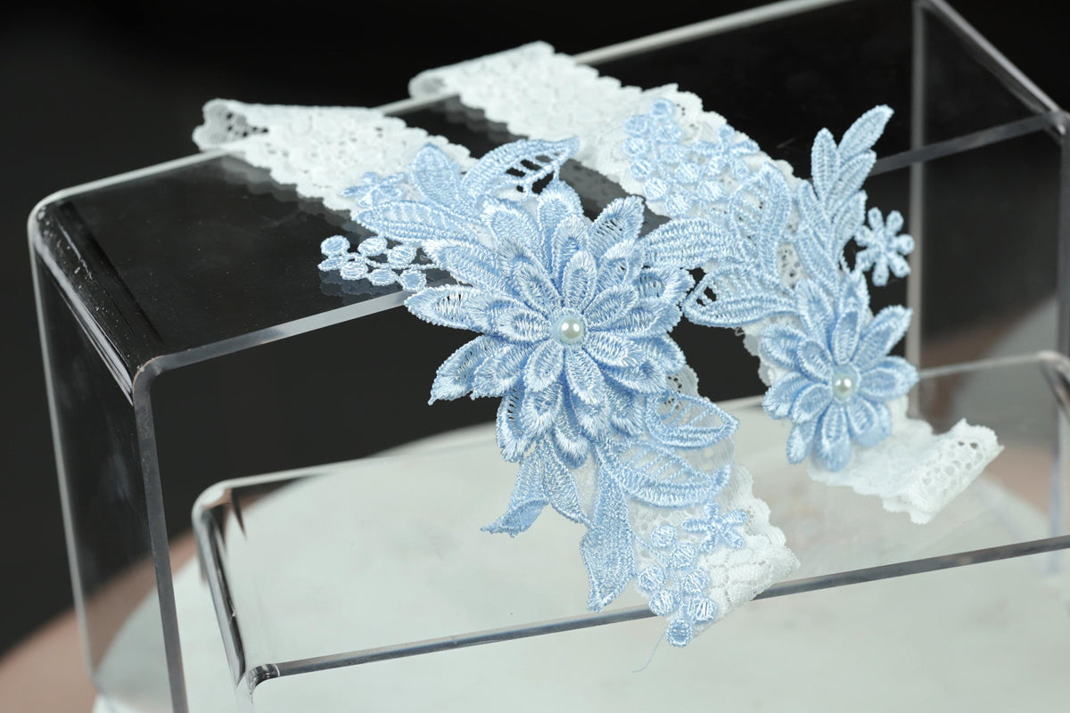 A clear glass display case containing a delicate, lace-like accessory with blue floral patterns.