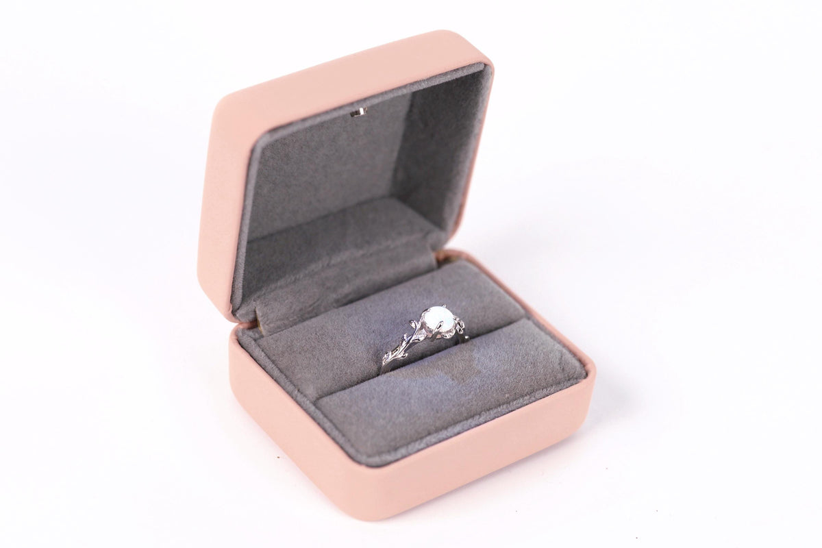 A pink jewelry box containing a silver ring with a large central stone.