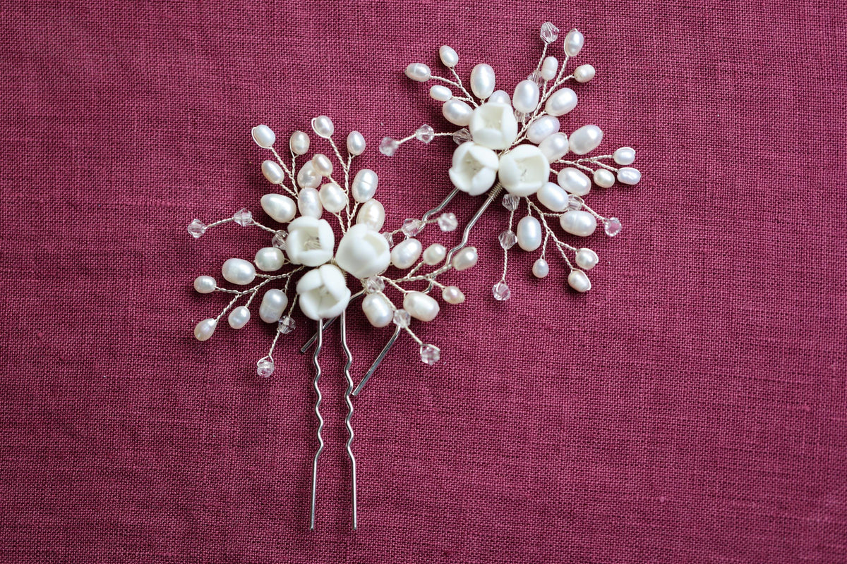 two white flower-shaped hair clips with pearl-like embellishments, placed on a red fabric background.