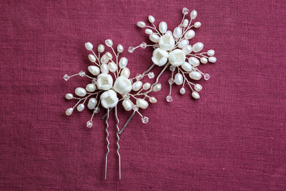 two white flower-shaped hair clips with pearl-like embellishments, placed on a red fabric background.