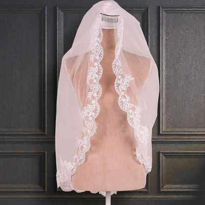 A white wedding veil with a delicate lace trim is displayed on a mannequin against a dark wooden panel backdrop.