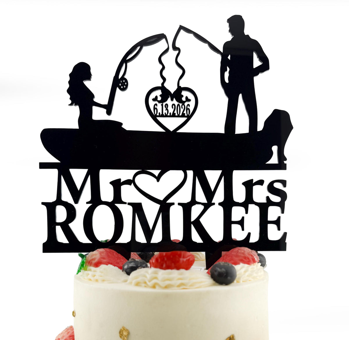 A silhouette of a man and a woman fishing on a boat, with the date "6.13.2026" displayed above them. The silhouette is part of a decorative cake topper that says "Mr. ROMKEE" and features a heart symbol.