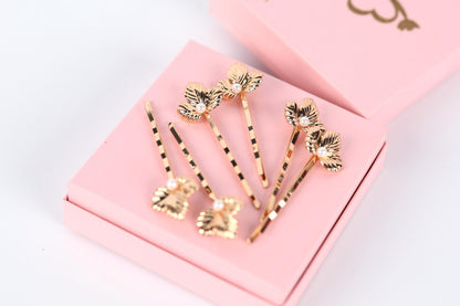 A pink box containing several gold hair clips with leaf-shaped designs.
