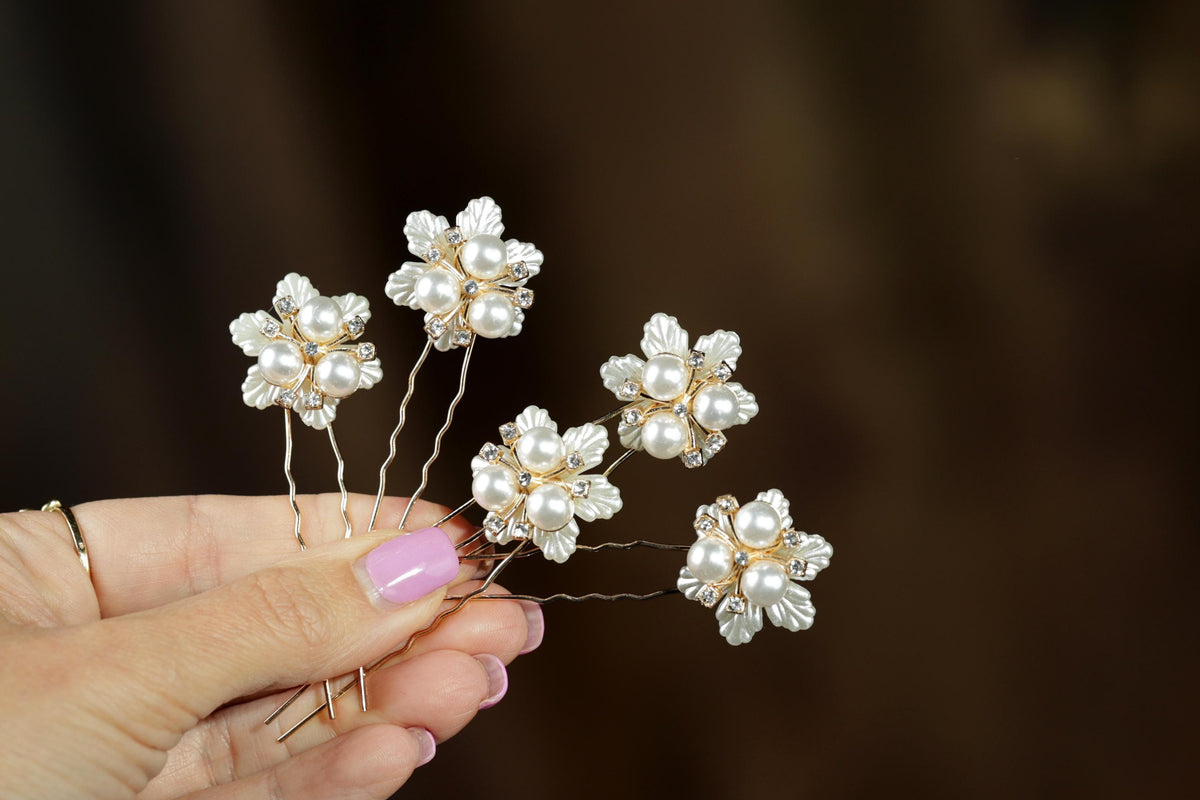 A hand holding a group of ornate hair clips with white flowers and gemstones.