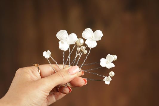 A hand holding a bunch of white flowers with small pearls attached to them.
