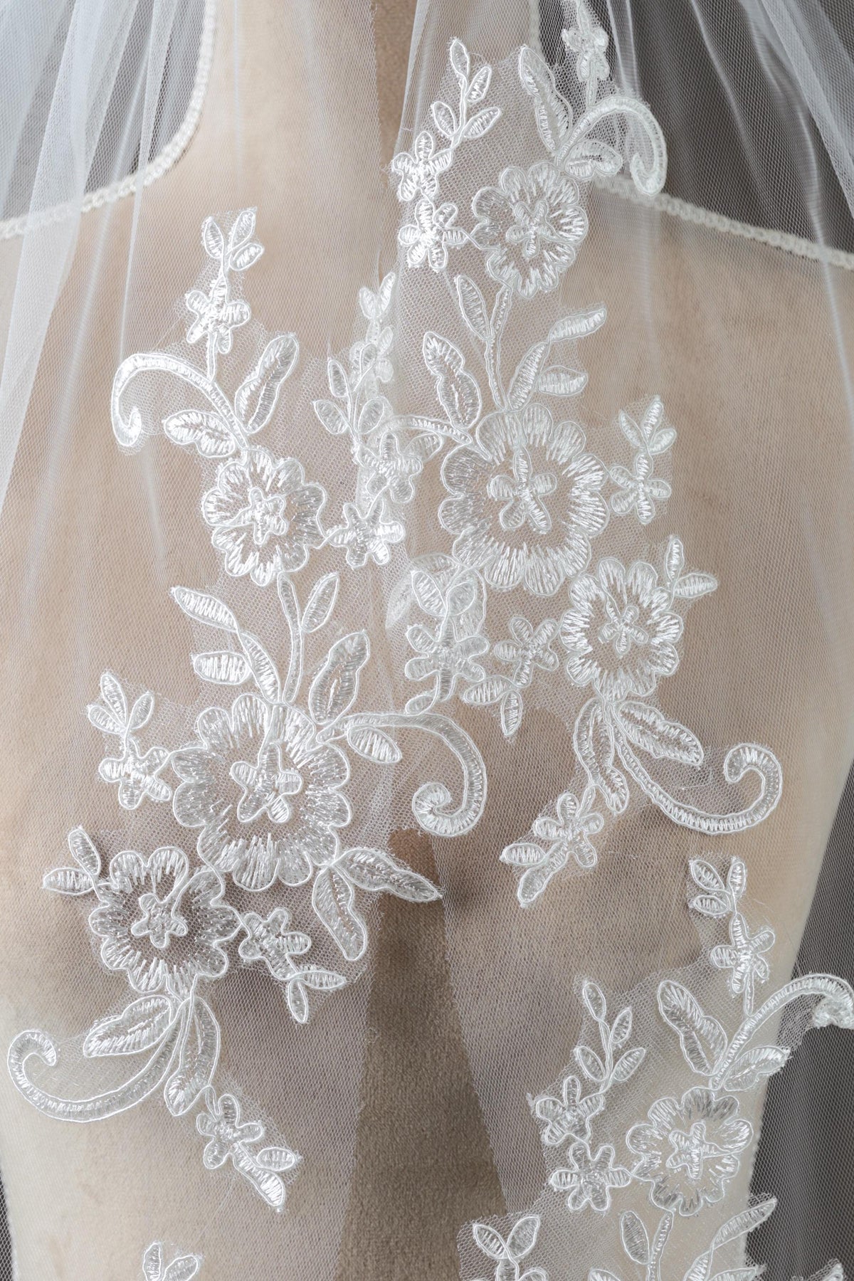 a close-up view of a delicate, white lace veil with intricate floral embroidery.