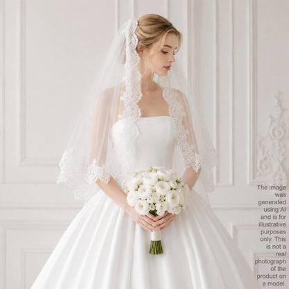 A woman in a white wedding dress holding a bouquet of white flowers stands in front of a white wall.