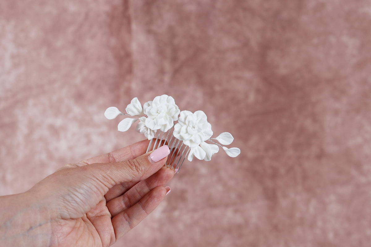 A hand holding a white flower hair accessory against a pink background.