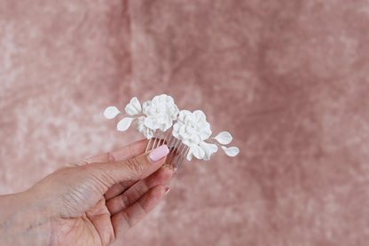 A hand holding a white flower hair accessory against a pink background.