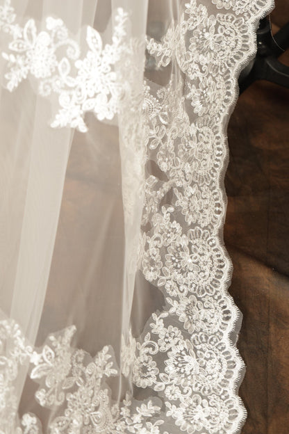 A close-up view of a delicate, white lace fabric with intricate floral embroidery.